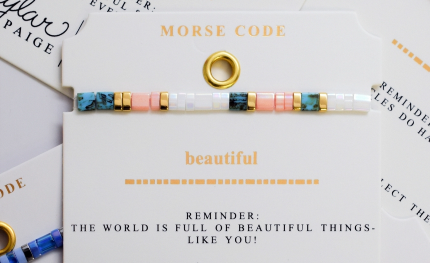 Sophisticated woman resting arms on gold chair, showcasing colorful and metallic tila bracelets spelling Morse code messages on her wrist. 