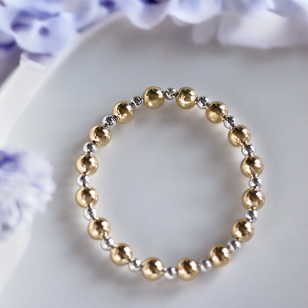 Alternating mixed-metal stretch bracelet features alternating 6mm 14k Gold-filled and 4mm sterling silver beads.surrounded by purple flowers.