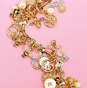 14k gold-filled Pandora Moments Smooth Snake Chain Bracelet adorned with exquisite charms including bees, zodiac symbols, a moon and stars motif, a key lock, and more, all set against a vibrant poppy pink background.