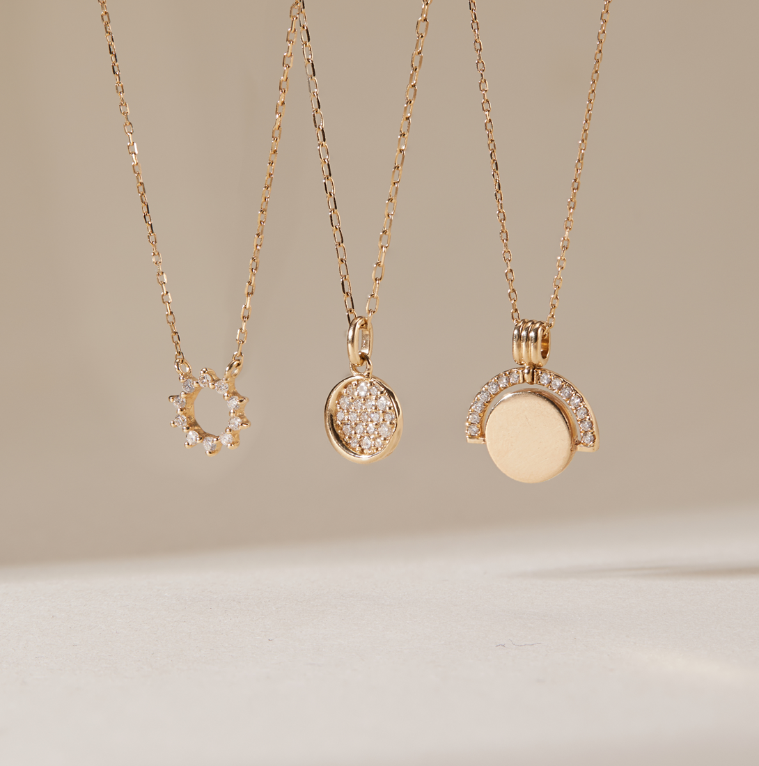 Aurelie Gi 14k gold and diamond necklaces featuring modern minimalist pendants — a sunburst circle, pavé diamond disc, and half-moon arc design. Dainty fine jewelry perfect for layering, everyday wear, or special occasions.