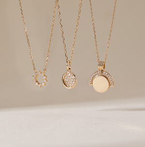 Aurelie Gi 14k gold and diamond necklaces featuring modern minimalist pendants — a sunburst circle, pavé diamond disc, and half-moon arc design. Dainty fine jewelry perfect for layering, everyday wear, or special occasions.
