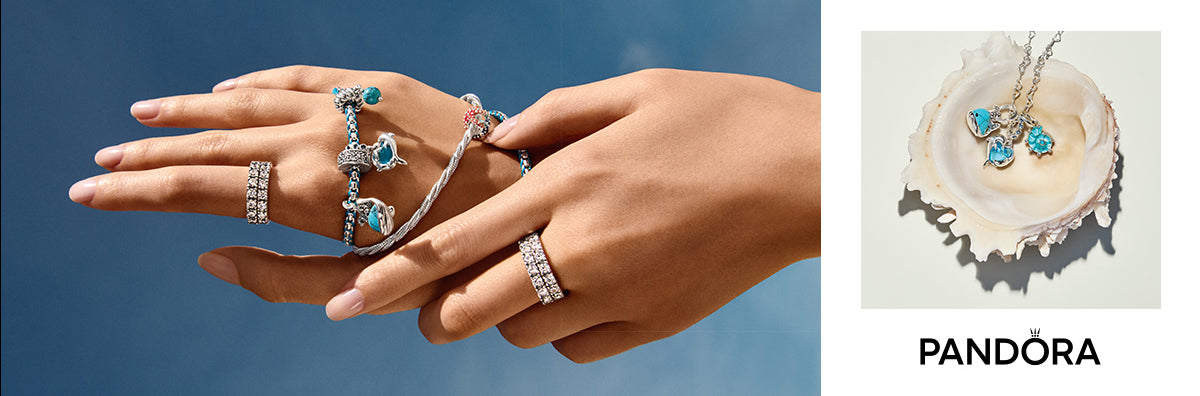 Pandora ocean-themed jewelry collection featuring silver charm bracelets with blue crystal dolphin and wave charms, pavé band rings, and a shell displaying matching sea-inspired pendant necklaces with turquoise and aqua accents, set against a coastal blue sky and seashell backdrop.