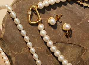 Luxurious autumn-inspired pearl jewelry set featuring a strand necklace with gold clasp, matching pearl stud earrings in gold settings, and baroque pearl strand, elegantly displayed on a rustic stone background.