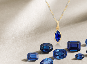Assorted blue sapphire gemstones with round halo sapphire stud earrings in white gold and a marquise-cut sapphire pendant necklace in yellow gold, displayed on a soft beige background – perfect for September birthstone or luxury gemstone jewelry promotions.