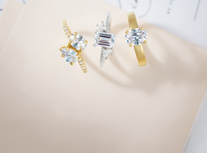 Elegant engagement rings featuring round and emerald-cut brilliant stones set in yellow gold and white gold bands, displayed on a soft neutral background for a luxury jewelry showcase.