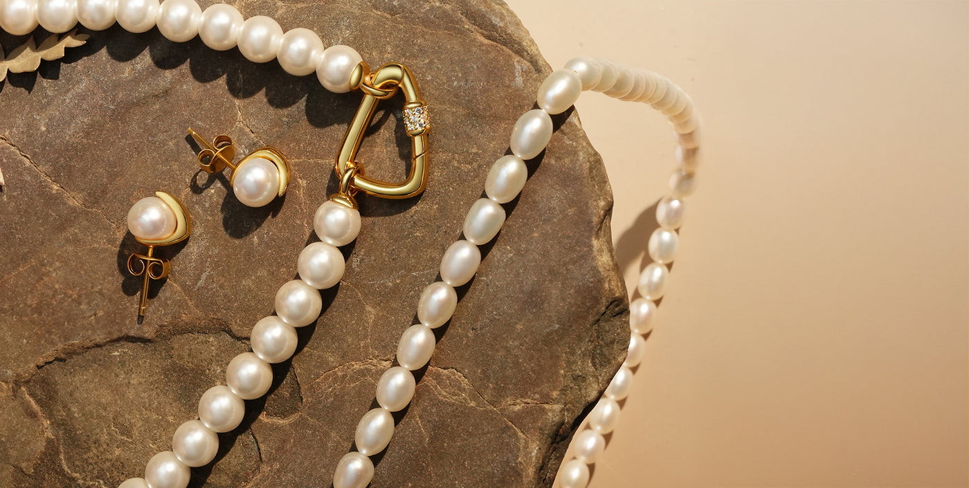 Luxurious autumn-inspired pearl jewelry set featuring a strand necklace with gold clasp, matching pearl stud earrings in gold settings, and baroque pearl strand, elegantly displayed on a rustic stone background.