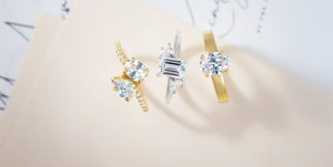 Elegant engagement rings featuring round and emerald-cut brilliant stones set in yellow gold and white gold bands, displayed on a soft neutral background for a luxury jewelry showcase.
