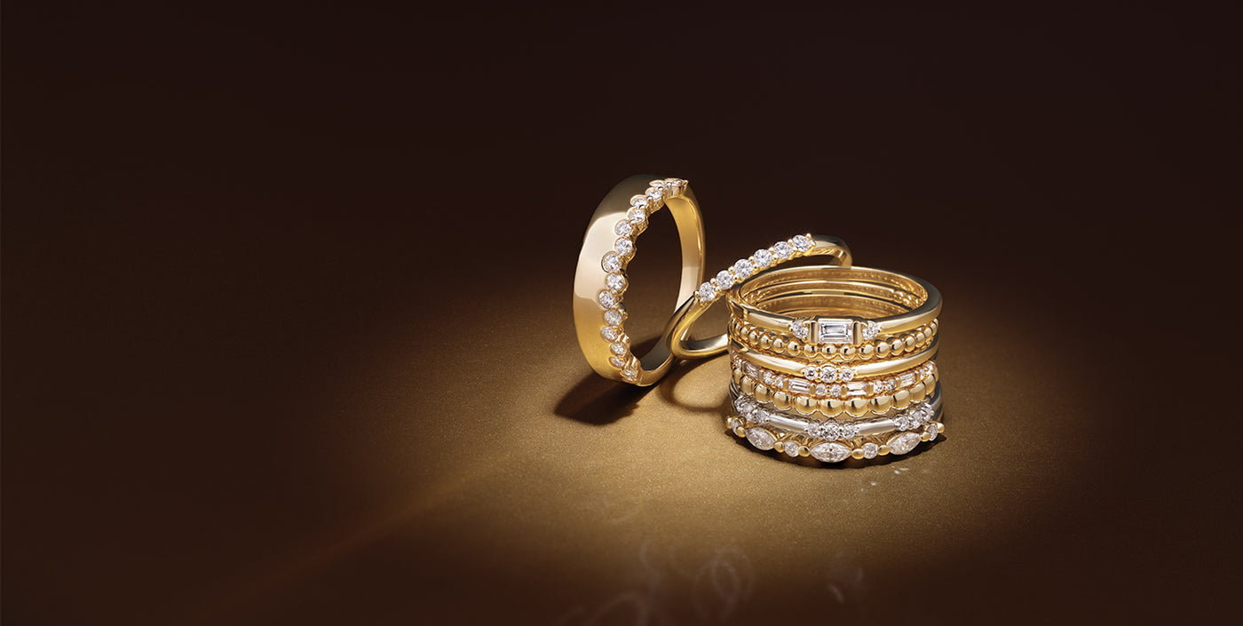 Stacked gold and diamond fine jewelry rings featuring round, marquise, and baguette-cut stones, set against a rich dark brown gradient background — luxury ring collection for elegant, timeless style.