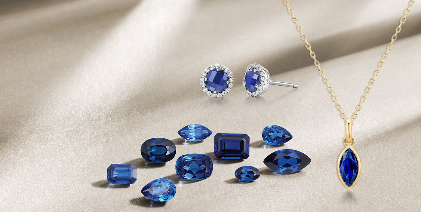 Assorted blue sapphire gemstones with round halo sapphire stud earrings in white gold and a marquise-cut sapphire pendant necklace in yellow gold, displayed on a soft beige background – perfect for September birthstone or luxury gemstone jewelry promotions.